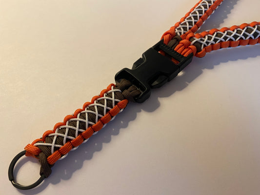 a close up of a brown and orange lanyard stitched with white microcord and made with black hardware.