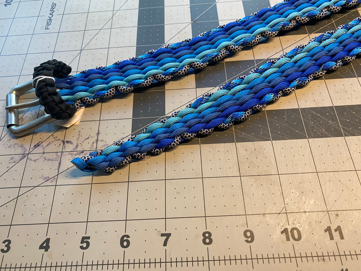 a belt built in shades of blue paracord with a black belt keeper and a silver buckle
