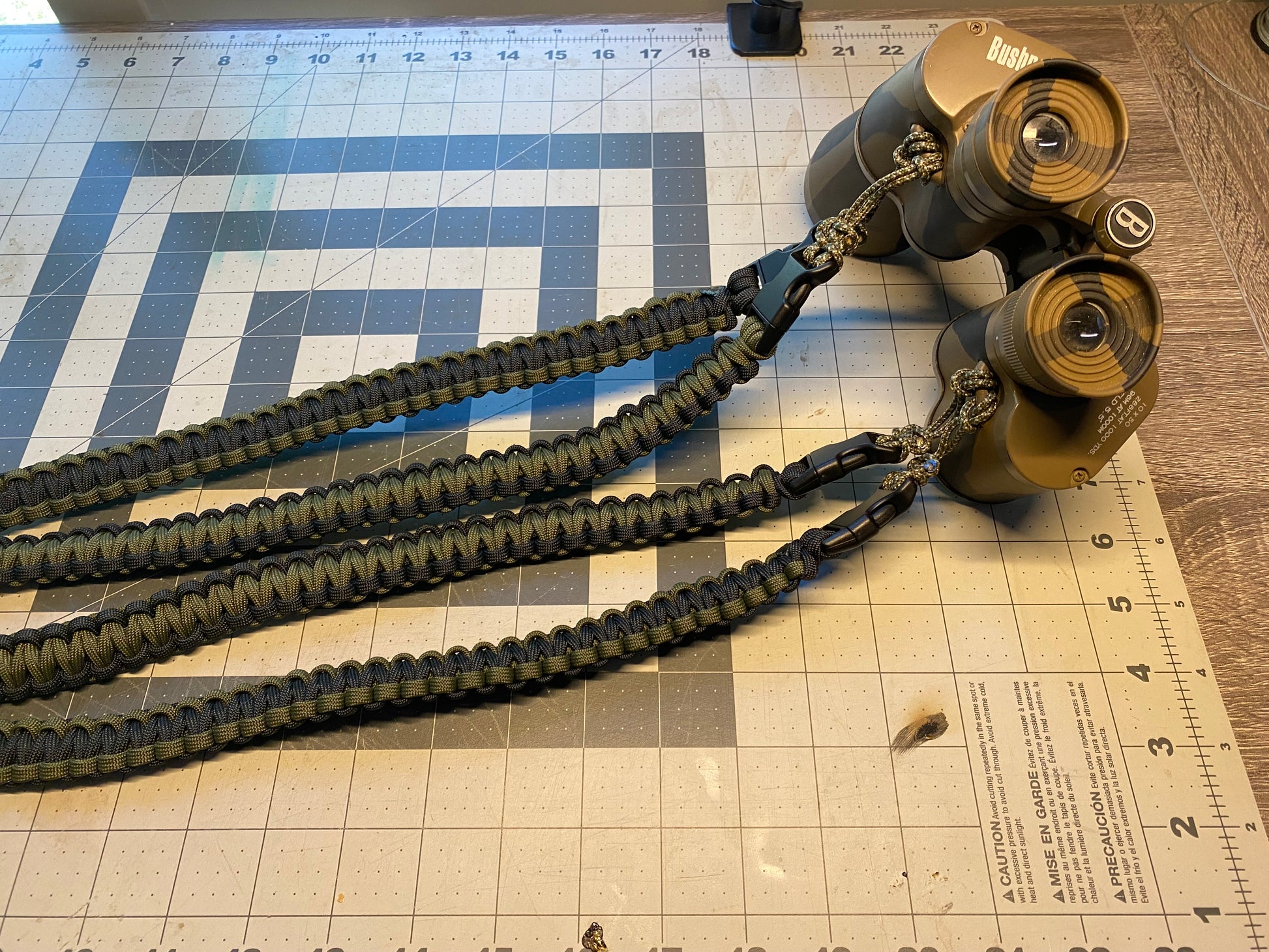 a binocular harness crafted from OD green and black 550 paracord attached to some binoculars