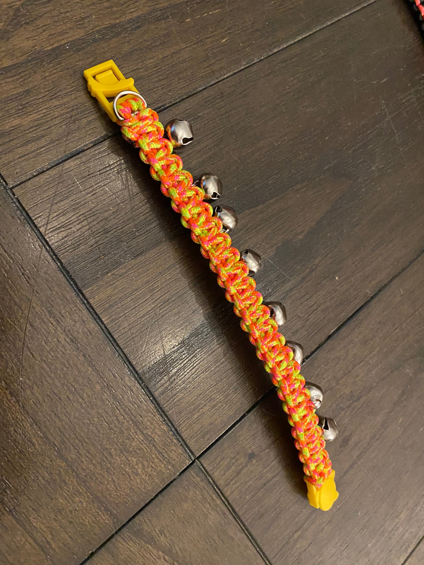 a cat collar with a break-away buckle made in a neon yellow, pink, and orange 275 paracord and with a bunch of bells