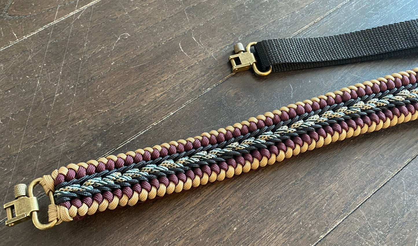 a fancy stitched modified sanctified gun sling made in tan, burgundy, and honor 550 paracord, black 275 cord, and brass trilock swivels