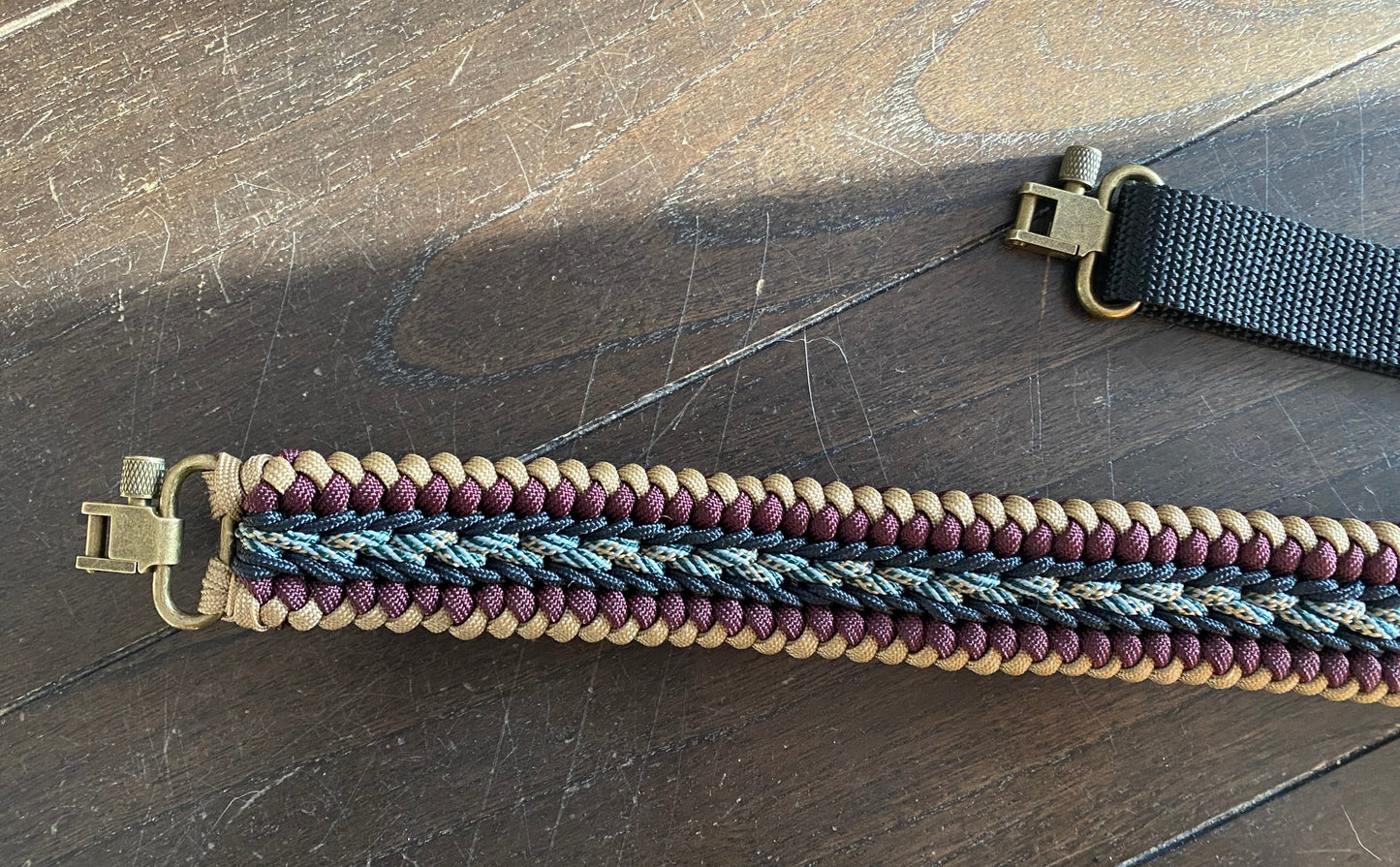 a fancy stitched modified sanctified gun sling made in tan, burgundy, and honor 550 paracord, black 275 cord, and brass trilock swivels