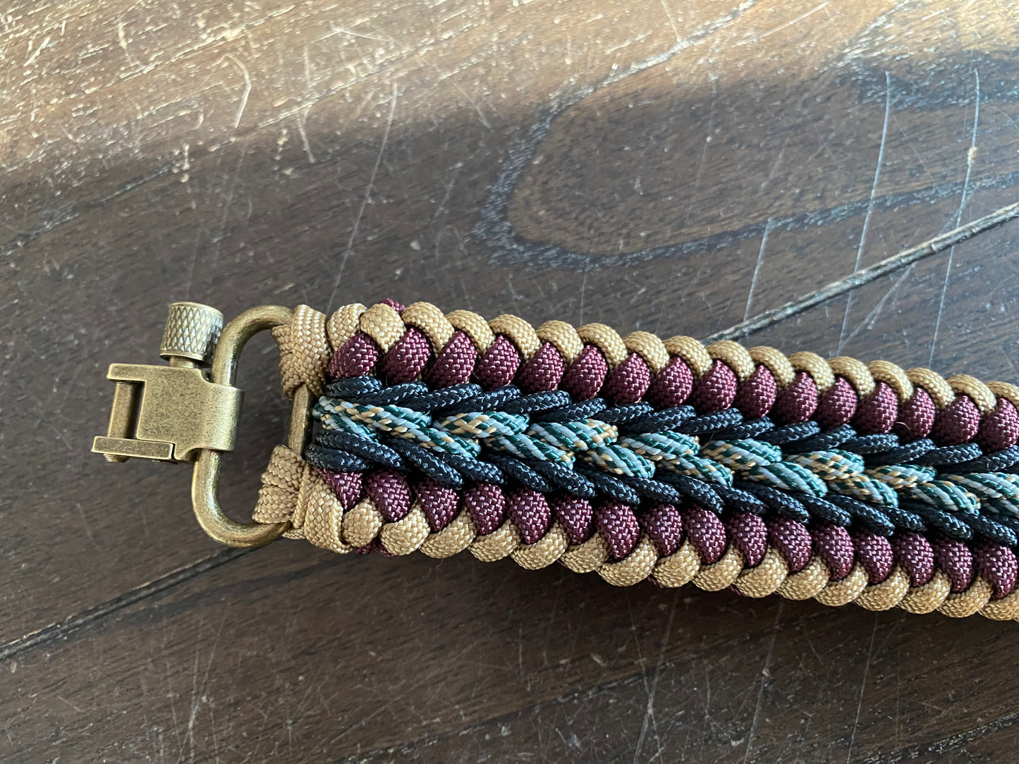 a fancy stitched modified sanctified gun sling made in tan, burgundy, and honor 550 paracord, black 275 cord, and brass trilock swivels