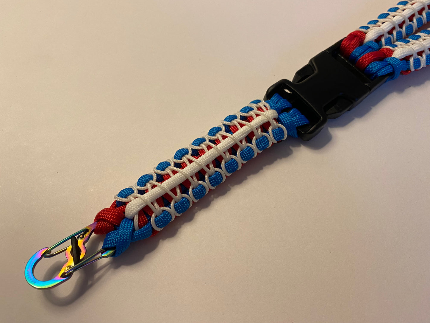 a close up of a herringbone stitched paracord lanyard made with patriotic red, white, and blue colors and black hardware.