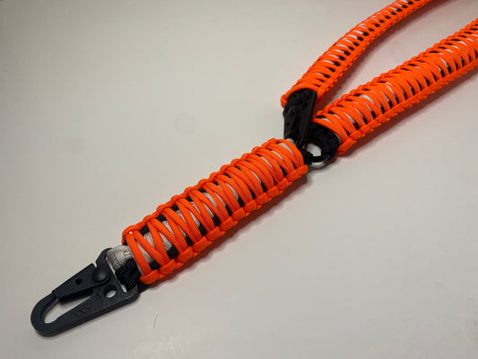 a single-point rifle sling made with neon orange, white, and black paracord in the double cobra weave with black hardware.