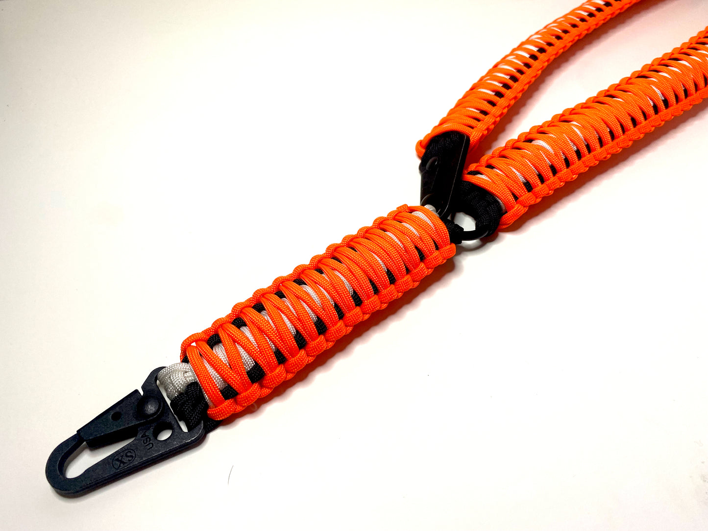 a single-point rifle sling made with neon orange, white, and black paracord in the double cobra weave with black hardware.
