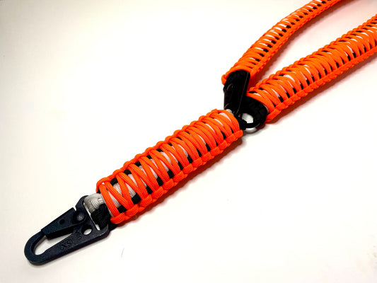 a single-point rifle sling made with neon orange, white, and black paracord in the double cobra weave with black hardware.