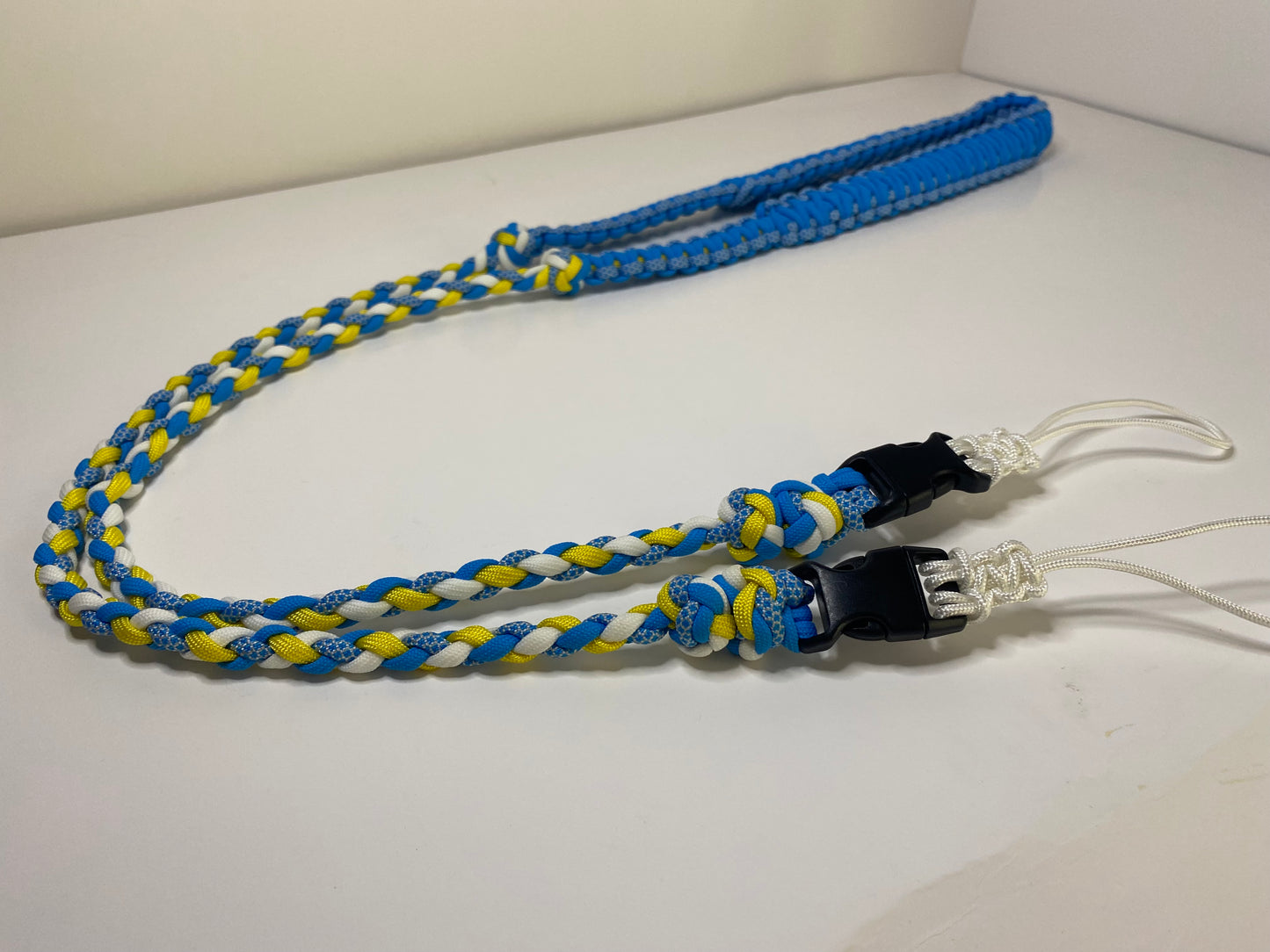 a fancy dual-weave paracord binocular lanyard with buckles made in light blue, yellow, and white cord.