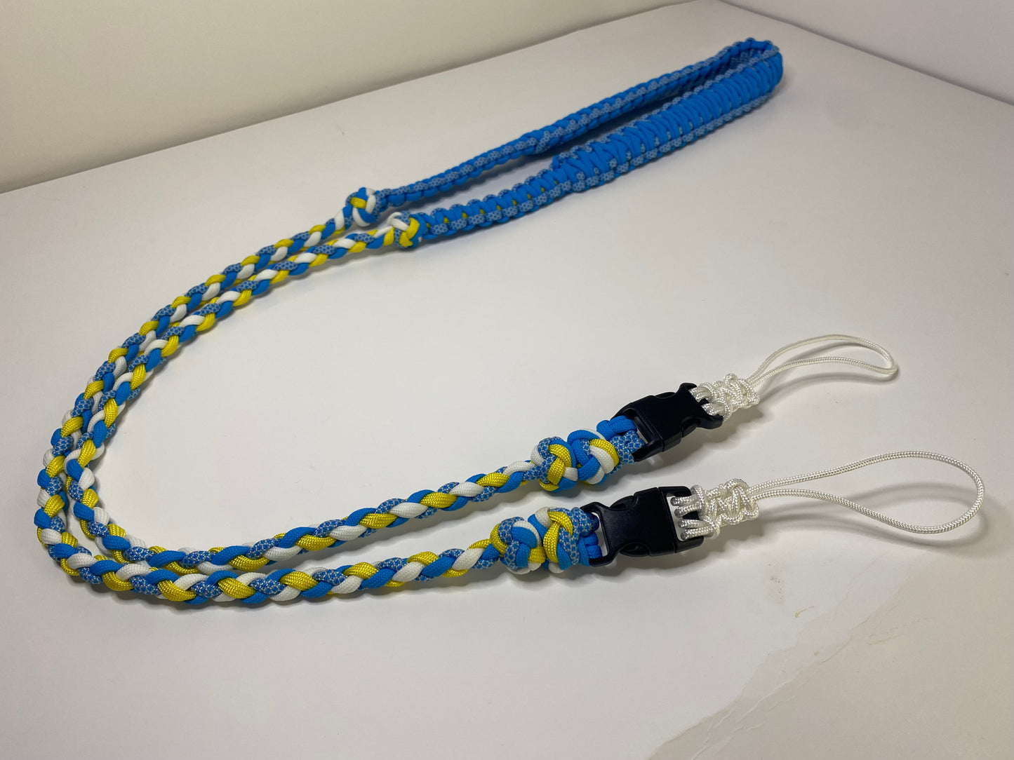 a fancy dual-weave paracord binocular lanyard with buckles made in light blue, yellow, and white cord.