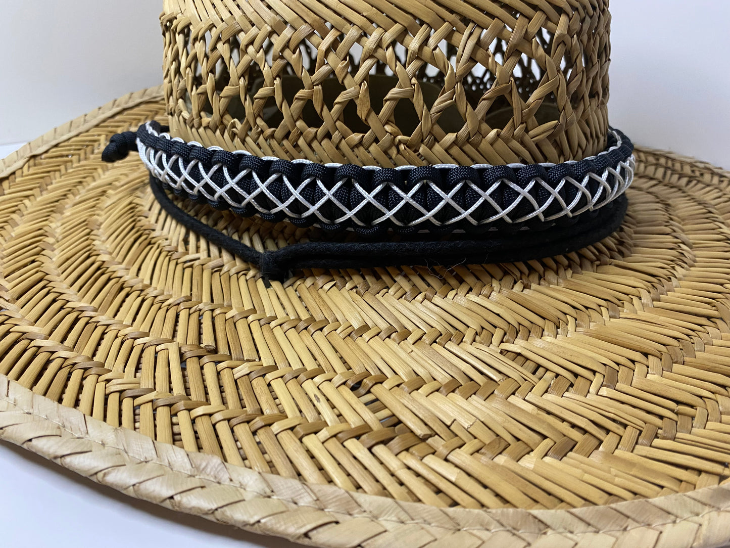 a hat band made in the cobra weave and made in black paracord and stitched with white microcord while attached to a straw hat.