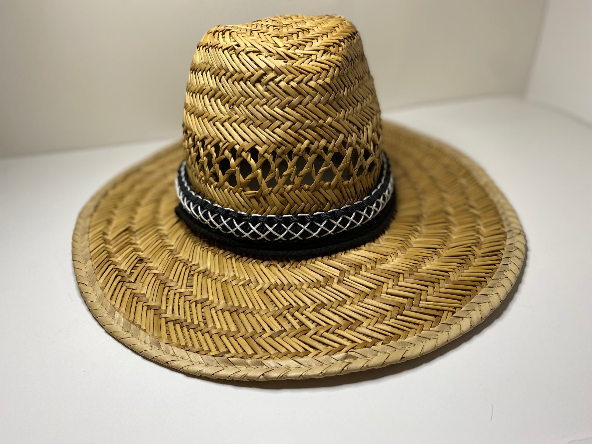 a hat band made in the cobra weave and made in black paracord and stitched with white microcord while attached to a straw hat.