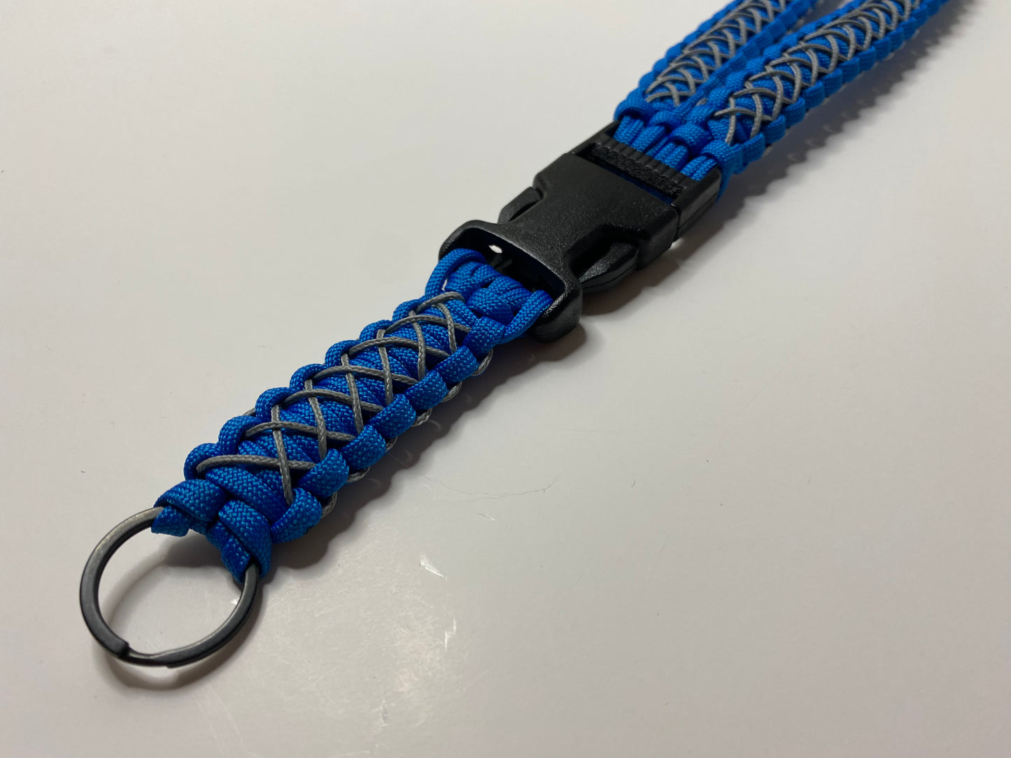 a close up of a general lanyard made with blue 550 paracord, black hardware, and stitched with grey microcord