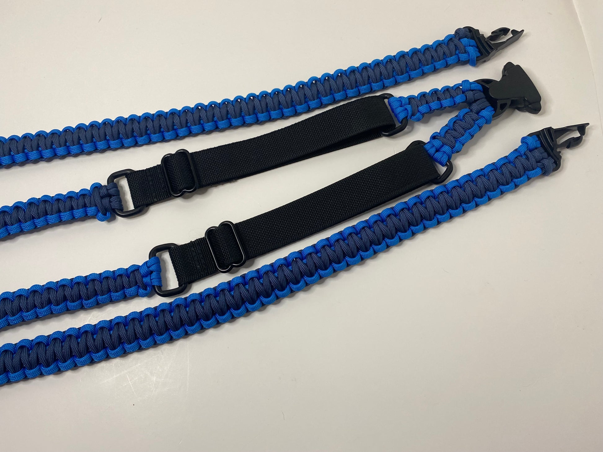 an adjustable paracord binocular harness made with blue and navy paracord and black hardware and webbing.