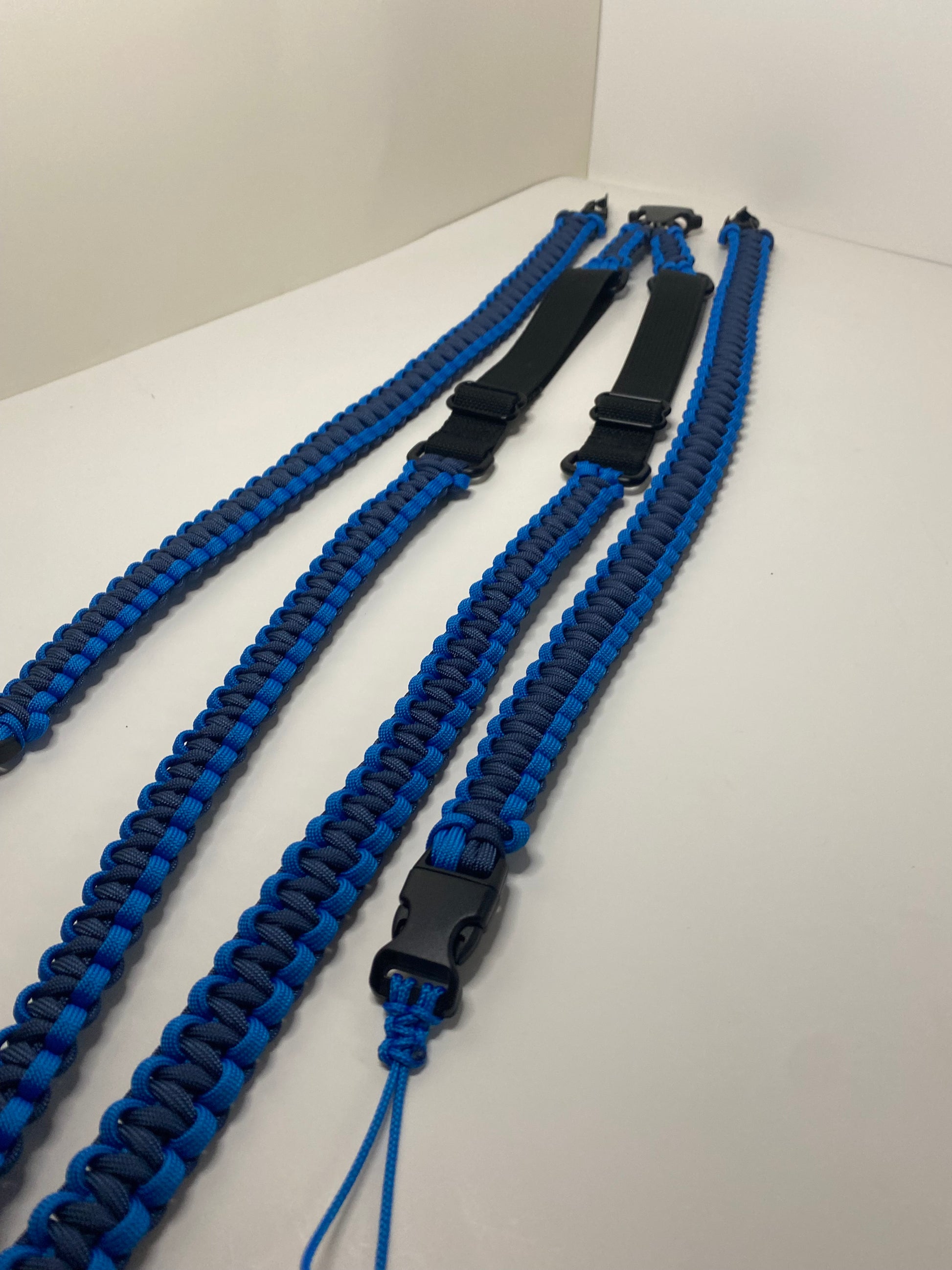 an adjustable paracord binocular harness made with blue and navy paracord and black hardware and webbing.