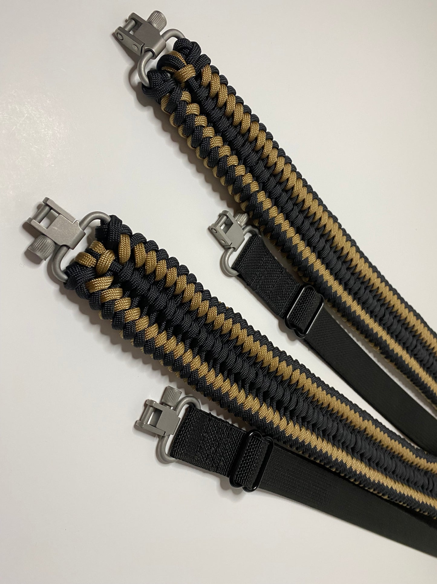 two rifle slings made in the sanctified covenant weave with black and tan paracord, black webbing and silver trilock swivels.