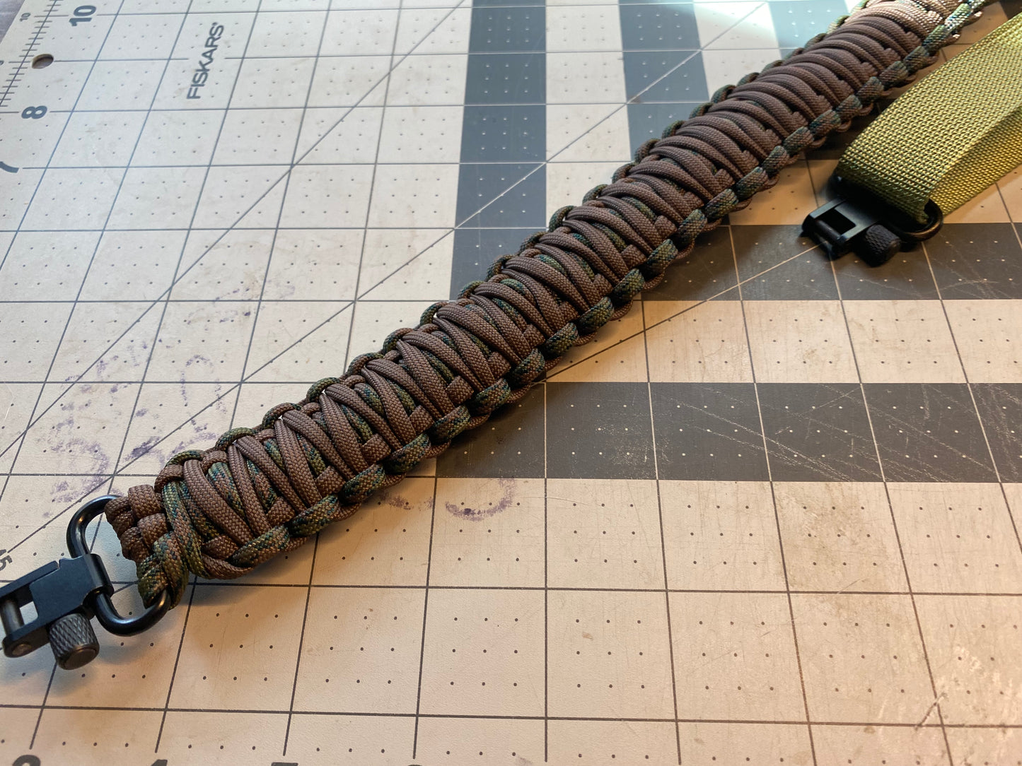 a brown and camo paracord rifle sling made with black hardware and OD green nylon webbing