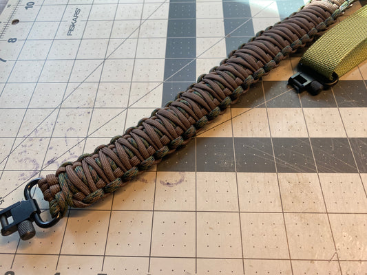 a brown and camo paracord rifle sling made with black hardware and OD green nylon webbing