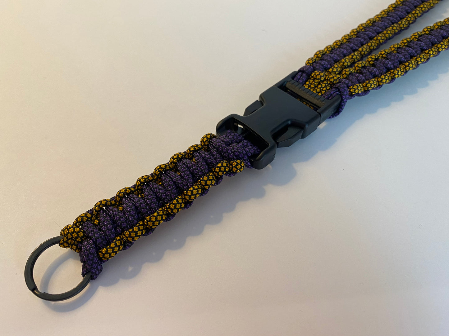 a general lanyard made with diamond patterned paracord colored gold and purple; made also with black hardware.