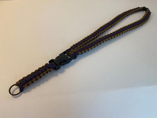 a general lanyard made with diamond patterned paracord colored gold and purple; made also with black hardware.