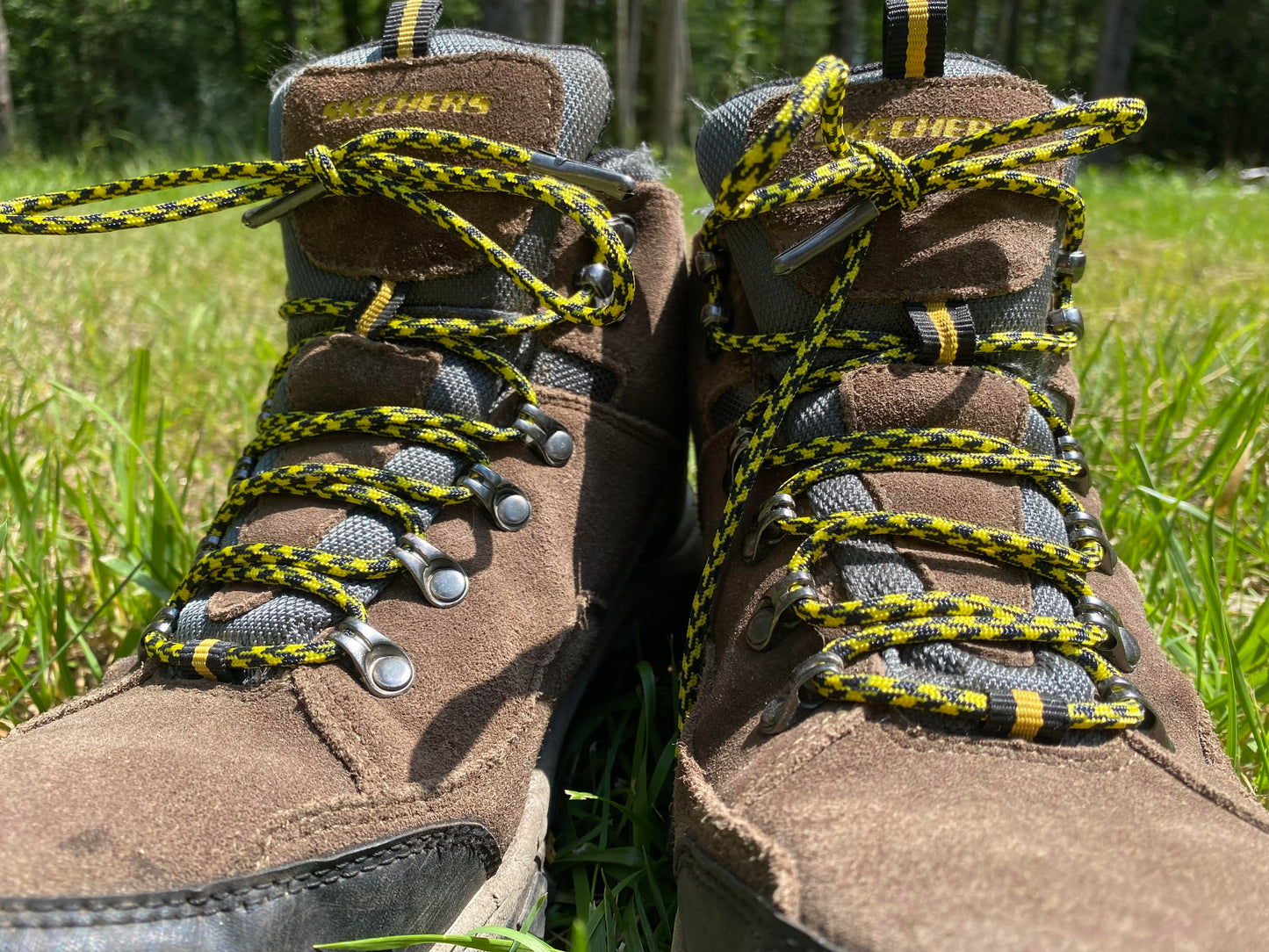 yellow and black 550 paracord bootlaces laced on a pair of boots sitting in the lush green summer grass