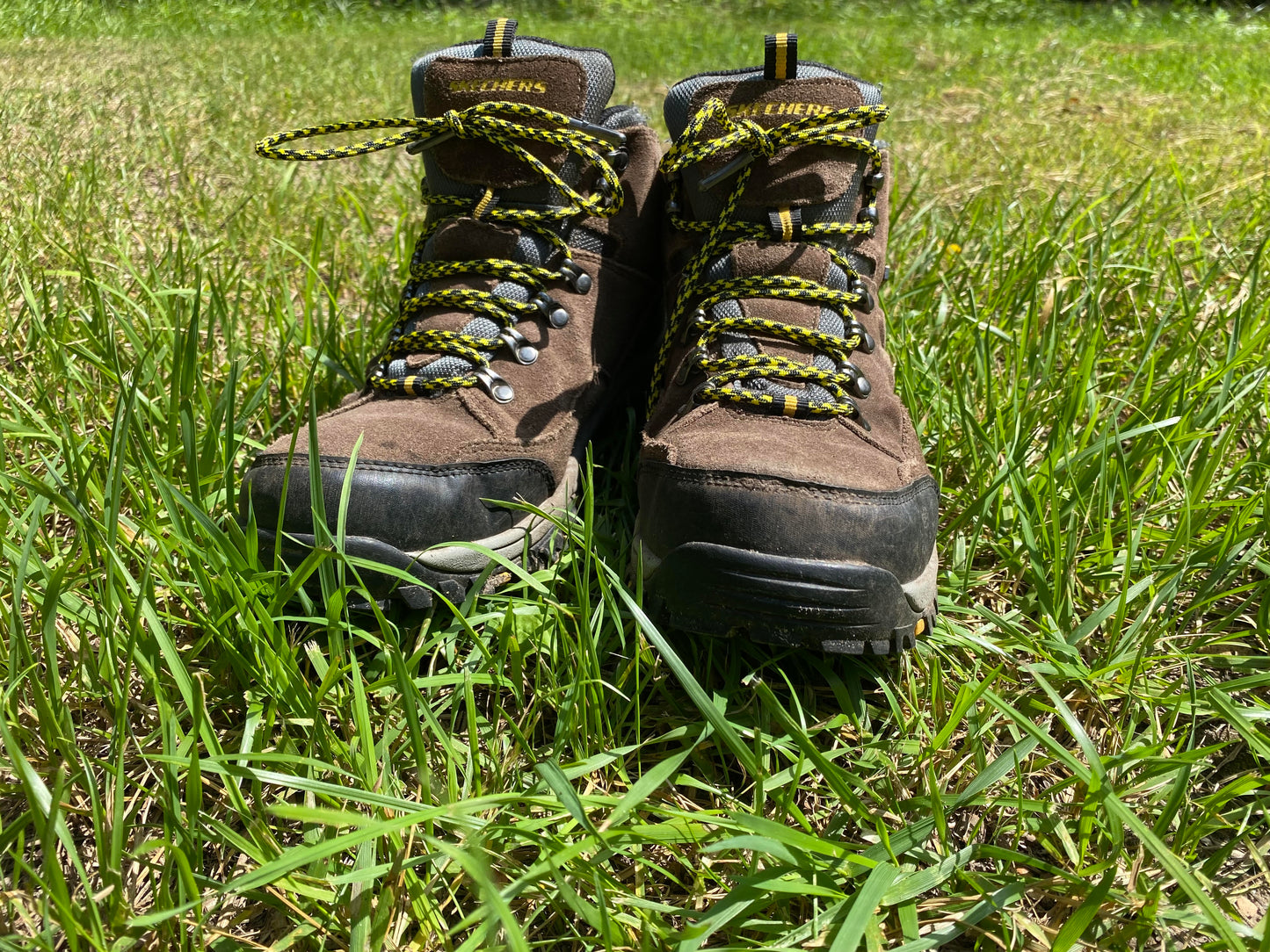 yellow and black 550 paracord bootlaces laced on a pair of boots sitting in the lush green summer grass