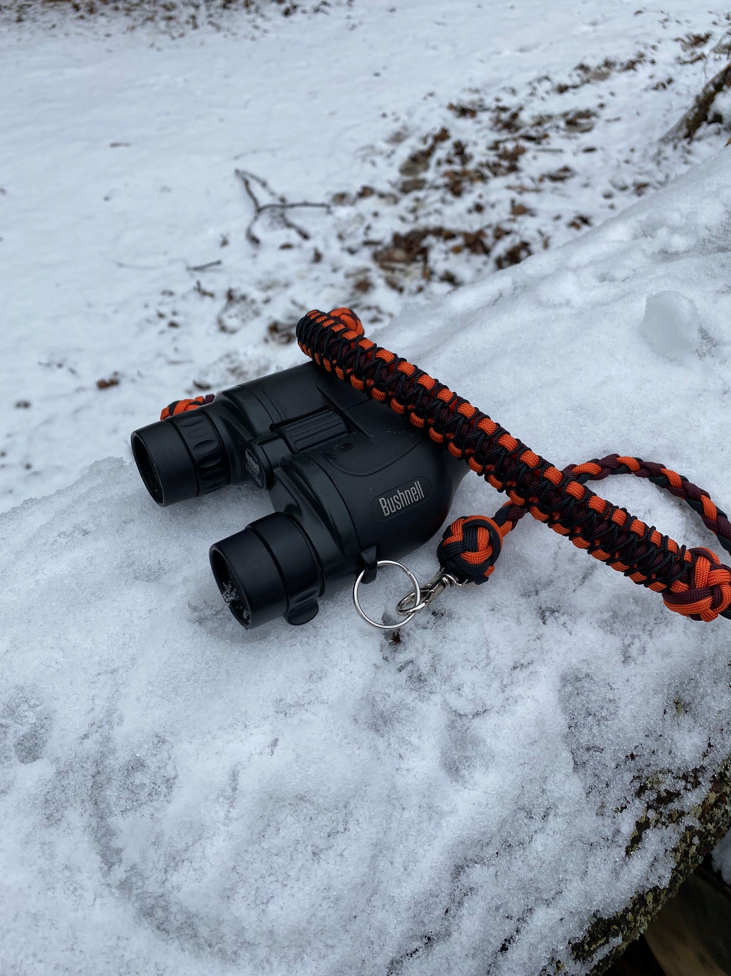 a 4-strand and cobra binocular lanyard attached to binoculars made with black, orange, burgundy paracord and stitched black microcord.