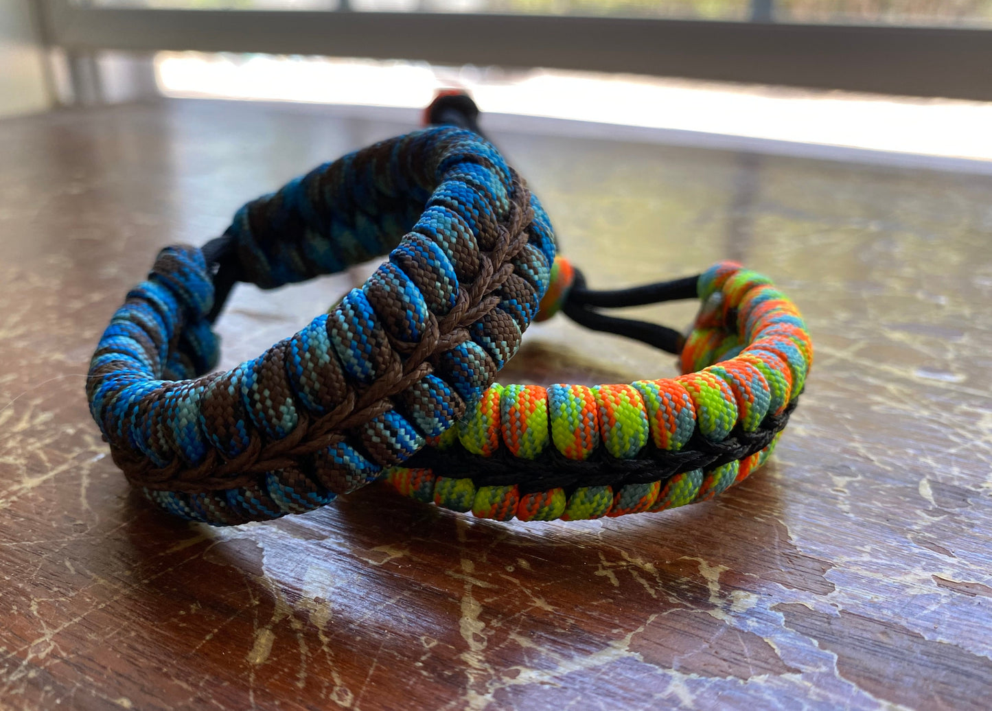 two adjustable fishtail bracelets sitting side by side made with colorful paracord and center-stitched with microcord.