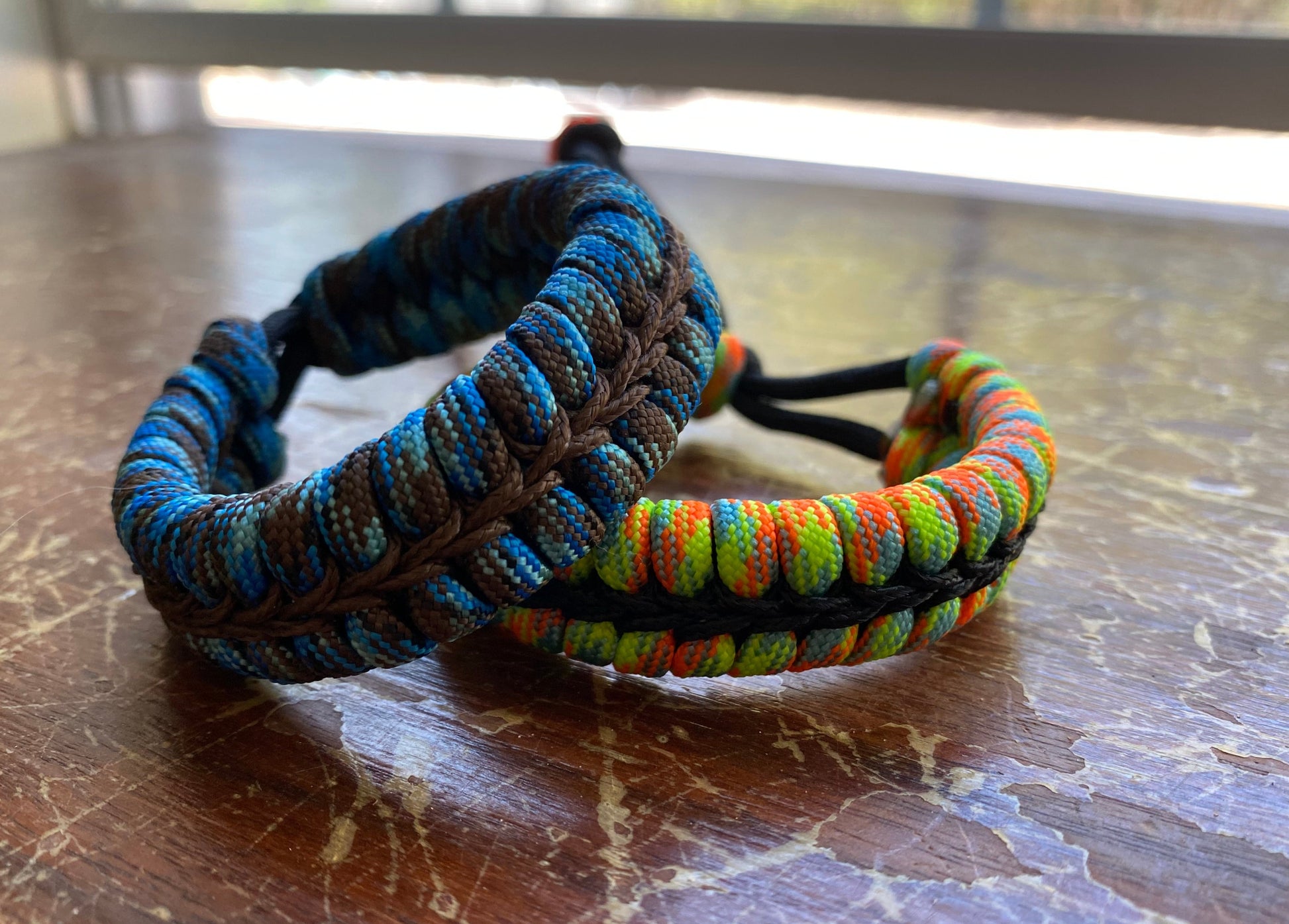 two adjustable fishtail bracelets sitting side by side made with colorful paracord and center-stitched with microcord.
