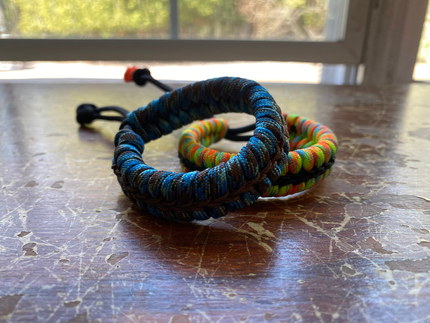 two adjustable fishtail bracelets sitting side by side made with colorful paracord and center-stitched with microcord.
