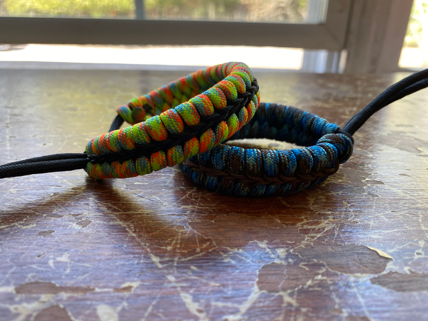 two adjustable fishtail bracelets sitting side by side made with colorful paracord and center-stitched with microcord.