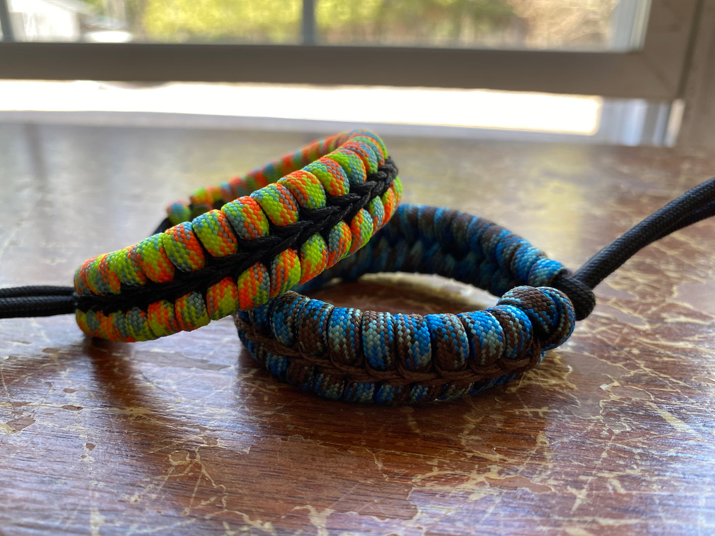 two adjustable fishtail bracelets sitting side by side made with colorful paracord and center-stitched with microcord.