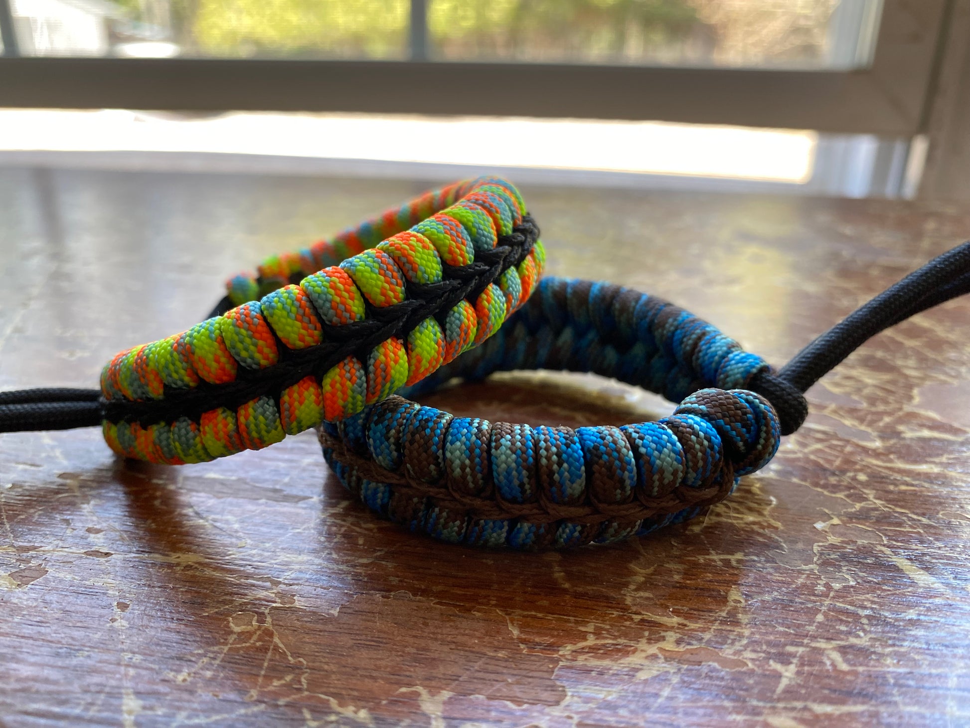 two adjustable fishtail bracelets sitting side by side made with colorful paracord and center-stitched with microcord.