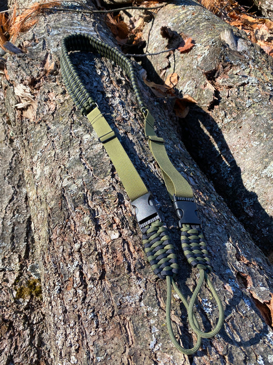 a trilobite woven bow sling made in OD green and black colors sitting on a log in the sun.