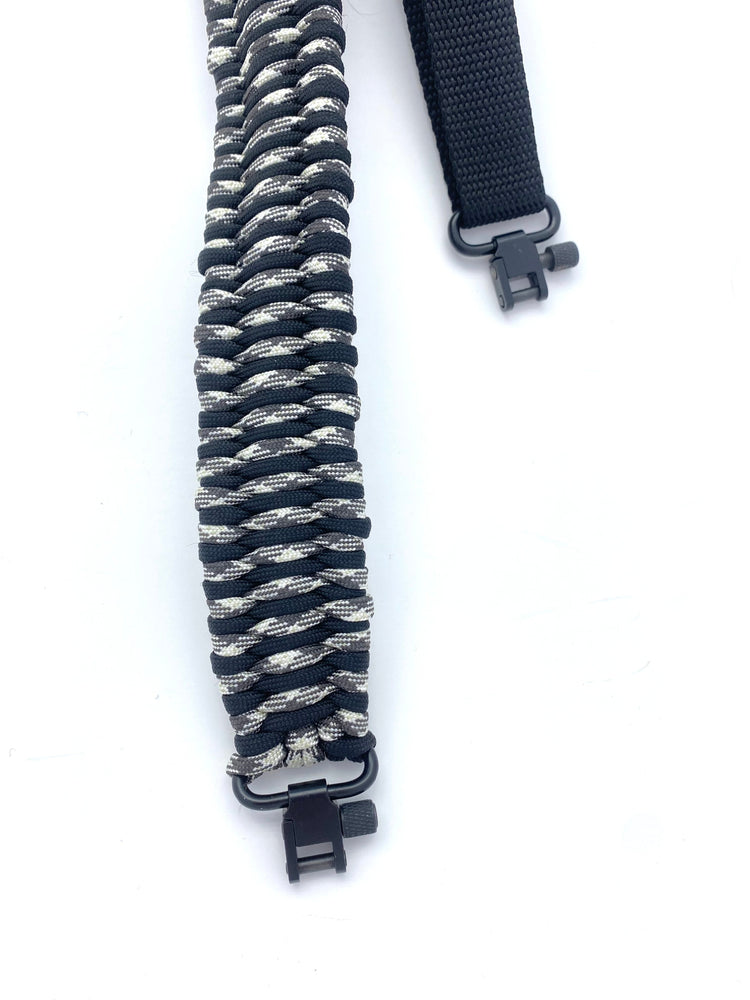 a handmade rifle sling constructed with black and arctic camo paracord and black hardware and webbing